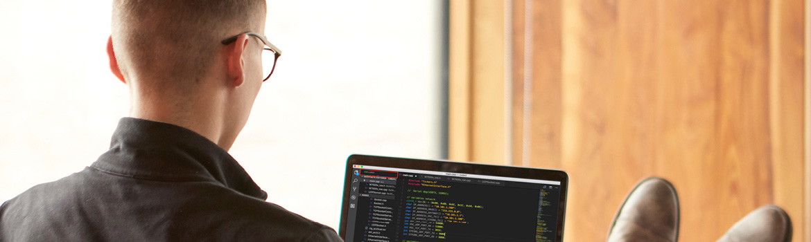 Student working on laptop while lounging in a chair, looking at code on a laptop screen.